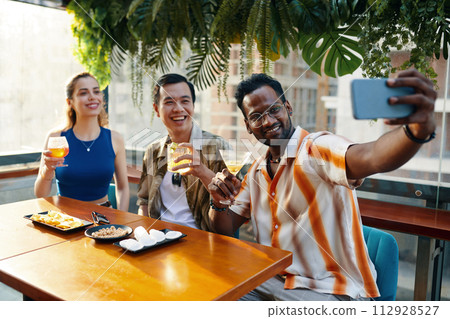 Excited man taking selfie with friends when sitting at table in bar 112928527