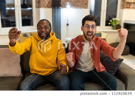 Two friends spending time together watching tv and looking excited Two friends spending time together watching tv and looking excited 112928639