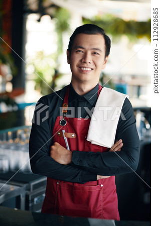 Smiling Vietnamese bartender with towel on shoulder working in restaurant Smiling Vietnamese bartender with towel on shoulder working in restaurant 112928685