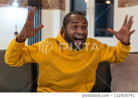 Dark-skinned man in yellow hoodie looking excited 112928741