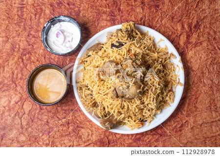 Indian famous mutton biryani dish served on white plate is delicious and fragrant with raita and gravy. 112928978