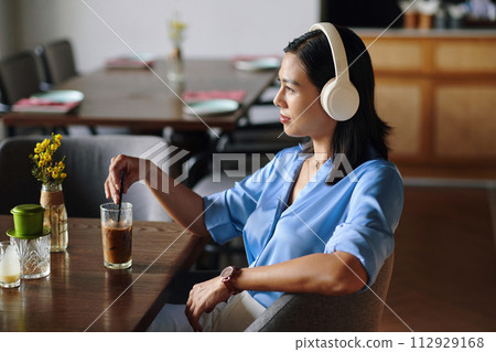 Pensive woman listening to music in headphones and drinking iced coffee in cafe 112929168