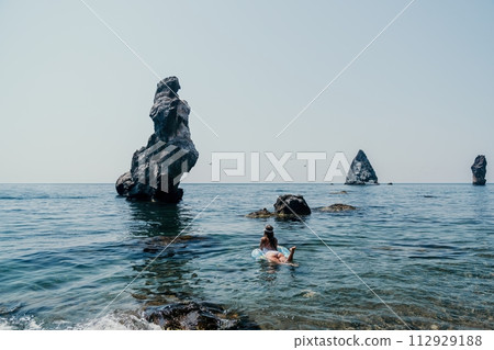 Woman summer sea. Happy woman swimming with inflatable donut on the beach in summer sunny day, surrounded by volcanic mountains. Summer vacation concept. Woman summer sea. Happy woman swimming with inflatable donut on the beach in summer sunny day, surrounded by volcanic mountains. Summer vacation concept. 112929188