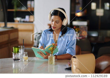 Businesswoman in headphones writing down plans and ideas Businesswoman in headphones writing down plans and ideas 112929189
