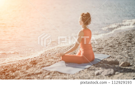 Woman sea yoga. Selective focus. Young beautiful caucasian woman in a red suit practicing yoga on the beach at sunrise near the sea. Yoga. Healthy lifestyle. Meditation concept. Woman sea yoga. Selective focus. Young beautiful caucasian woman in a red suit practicing yoga on the beach at sunrise near the sea. Yoga. Healthy lifestyle. Meditation concept. 112929193