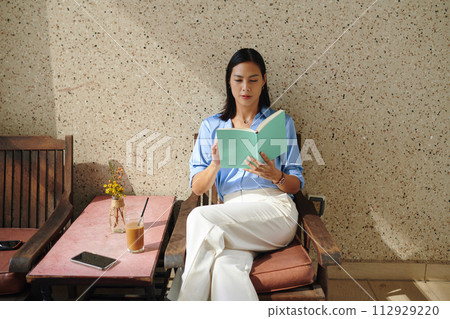 Elegant woman relaxing in coffeeshop, drinking iced coffee and reading book Elegant woman relaxing in coffeeshop, drinking iced coffee and reading book 112929220