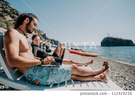 Man woman laptop sea. Working remotely on seashore. Happy successful couple, freelancers working on sea beach, relieves stress from work to restore life balance. Freelance, remote work on vacation 112929238