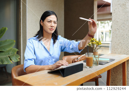 Creative woman sitting at cafe table and drawing sketch on tablet computer 112929244