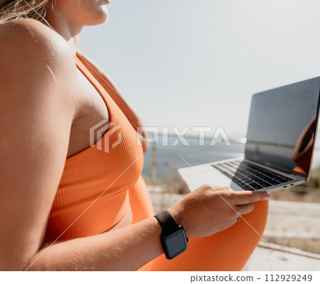 Woman laptop sea. Working remotely on seashore. Happy successful woman female freelancer working on laptop by the sea at sunset, makes a business transaction online. Freelance, remote work on vacation 112929249