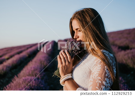 Woman lavender field. Happy carefree woman in a white dress walking in a lavender field and smelling a lavender bouquet on sunset. Ideal for warm and inspirational concepts in wanderlust and travel. Woman lavender field. Happy carefree woman in a white dress walking in a lavender field and smelling a lavender bouquet on sunset. Ideal for warm and inspirational concepts in wanderlust and travel. 112929253