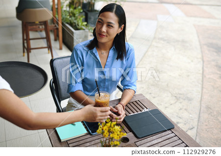 Waiter bringing iced coffee to happy businesswoman 112929276