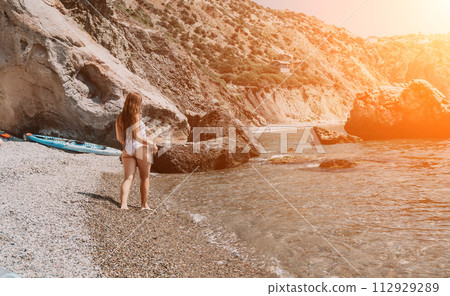 Woman travel sea. Happy tourist in white bikini enjoy taking picture outdoors for memories. Woman traveler posing on the beach at sea surrounded by volcanic mountains, sharing travel adventure journey Woman travel sea. Happy tourist in white bikini enjoy taking picture outdoors for memories. Woman traveler posing on the beach at sea surrounded by volcanic mountains, sharing travel adventure journey 112929289
