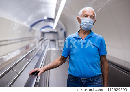 Senior man in mask standing on moving walkway Senior man in mask standing on moving walkway 112929893