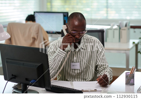 Bank manager answering phone call from client and taking notes in document Bank manager answering phone call from client and taking notes in document 112930115