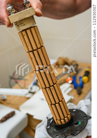 A man holds a dry ceramic heating element from a boiler in his hands. 112930307
