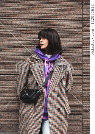 Portrait of young brunette woman wearing stylish casual coat and bright hoodie, posing against urban architecture 112931638