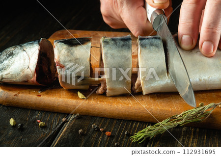 Close-up of a cook hands cutting mackerel fish with a knife before frying. The concept of preparing a fish menu for lunch with spices 112931695