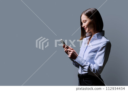 Young confident woman with smartphone in hands on grey studio background 112934434
