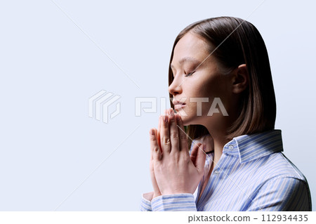 Close-up profile view of young woman with folded hands on white background 112934435