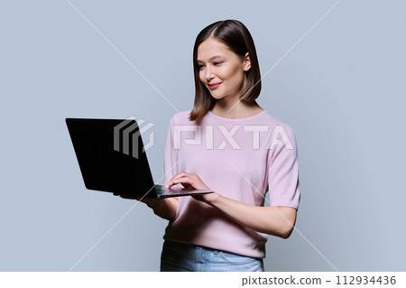 Smiling young woman with laptop on grey studio background 112934436