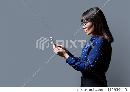 Profile view middle aged woman using smartphone on grey background 112934443
