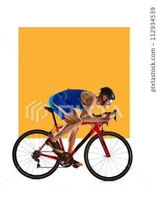 Concentrated and motivated man in sportswear and helmet, bicyclist in motion, training on white background with yellow element. Concentrated and motivated man in sportswear and helmet, bicyclist in motion, training on white background with yellow element. 112934539