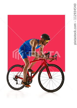 Concentrated and motivated man in sportswear and helmet, bicyclist in motion, training on white background with red element. Concentrated and motivated man in sportswear and helmet, bicyclist in motion, training on white background with red element. 112934540