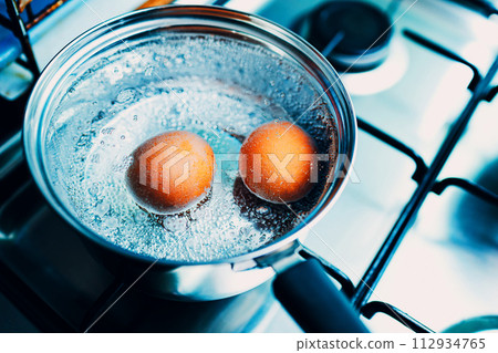 Saucepan stainless steel with two boiling eggs breakfast in a water on a gas stove top view. 112934765