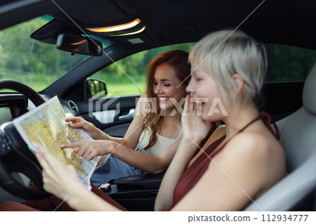 Happy young two women driver tourist travelers with paper map at rental car vehicle Happy young two women driver tourist travelers with paper map at rental car vehicle 112934777