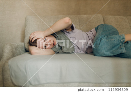 Young woman wearing scarf has flu ill sick disease cold at home indoor lying on sofa Young woman wearing scarf has flu ill sick disease cold at home indoor lying on sofa 112934809