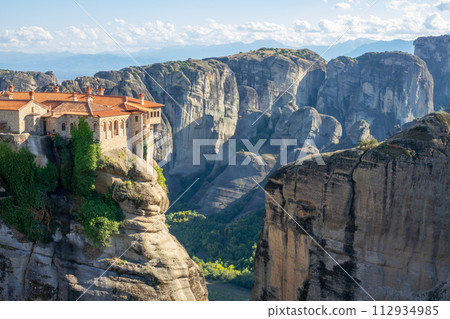 Greek Rock Monastery and Light Clouds over the Mountain Peaks 112934985