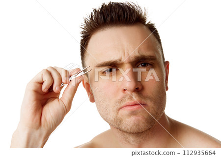 Young focused man with short brunette hair with tweezers looking at camera against white studio background. Young focused man with short brunette hair with tweezers looking at camera against white studio background. 112935664