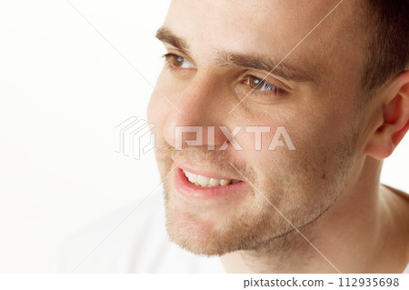 Close up portrait of smiling man with short hair and stubble, looking to side against white studio background. Close up portrait of smiling man with short hair and stubble, looking to side against white studio background. 112935698