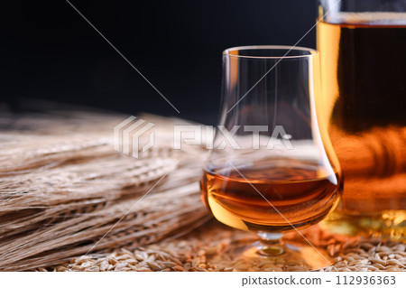 A glass of whiskey with bottle and barley ears on barley grains 112936363