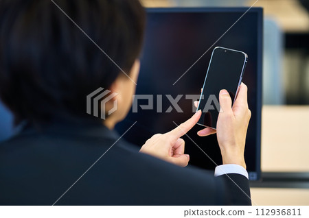 一位身著西裝的年輕商人在辦公室的辦公桌上操作智能手機 112936811