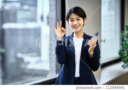 Middle business woman in a suit operating a smartphone in the office 112936991