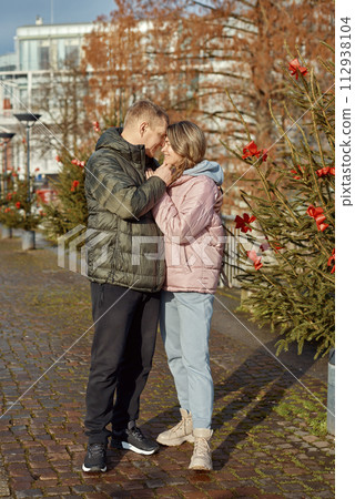 Portrait of young attractive people, lovely couple enjoying cozy atmosphere on fair in Christmas Eve. Spending time together. Concept of national traditions, winter holidays, fashion, festivities Portrait of young attractive people, lovely couple enjoying cozy atmosphere on fair in Christmas Eve. Spending time together. Concept of national traditions, winter holidays, fashion, festivities 112938104