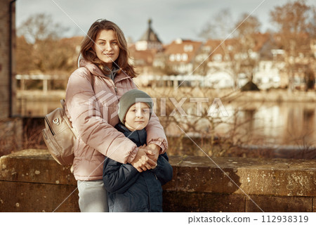 Riverside Family Harmony: Mother, 30 Years Old, and Son - Beautiful 8-Year-Old Boy, Standing by Neckar River and Historic Half-Timbered Town, Bietigheim-Bissingen, Germany, Autumn Riverside Family Harmony: Mother, 30 Years Old, and Son - Beautiful 8-Year-Old Boy, Standing by Neckar River and Historic Half-Timbered Town, Bietigheim-Bissingen, Germany, Autumn 112938319