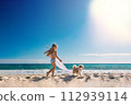 Little girl playing with a puppy on the beach at the seashore with blue sky background 112939114