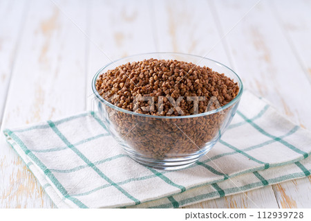Raw buckwheat in a glass plate on a white wooden table. Raw buckwheat in a glass plate on a white wooden table. 112939728