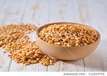 Dry yellow peas are scattered out of the wooden bowl on a light table, selective focus. 112939748