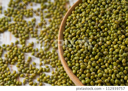 Mung beans are scattered in a wooden bowl close up. 112939757