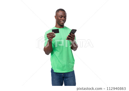 young american man dressed in green t-shirt and jeans uses smartphone and credit card 112940863
