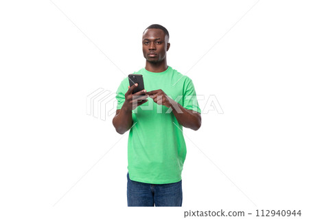 young american guy dressed in a mint t-shirt uses the phone on a white background with copy space young american guy dressed in a mint t-shirt uses the phone on a white background with copy space 112940944