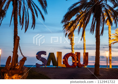 colorful letters of Salou town, palm trees andl beach at sunset, Catalonia, Spain colorful letters of Salou town, palm trees andl beach at sunset, Catalonia, Spain 112941722