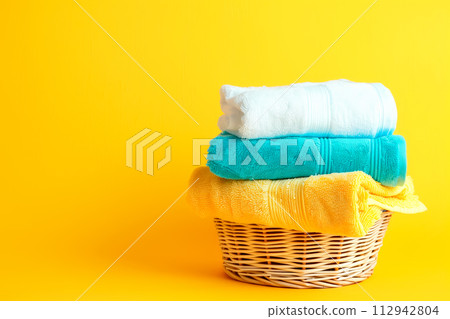 Stack of clean towels in laundry wicker basket on yellow background. The towels showcasing soft and fluffy textures 112942804
