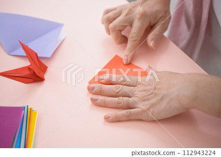 Hands of a middle-aged woman folding origami 112943224