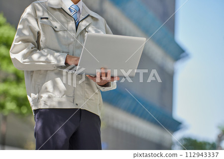 A man in work clothes looking at a computer at a construction site A man in work clothes looking at a computer at a construction site 112943337