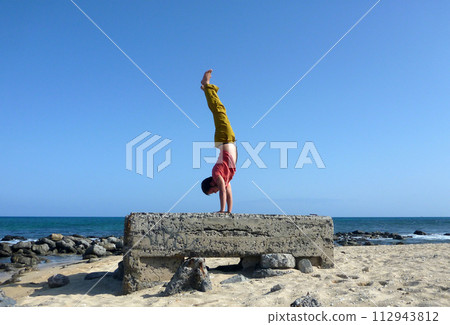 Man Handstands on top a old pillbox on the beach 112943812