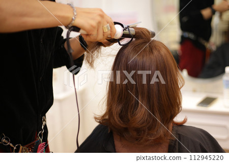 Male hairdresser ironing a woman's hair Male hairdresser ironing a woman's hair 112945220